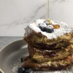 stack of strawberry jam-stuffed french toast with powdered sugar and syrup