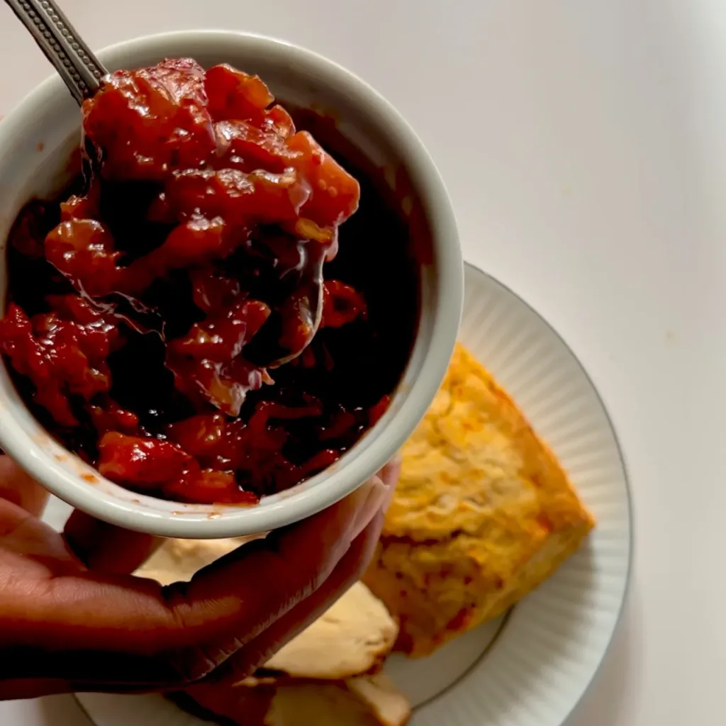 strawberry bacon and onion jam in a small white ramekin with sweet potato biscuit and turkey blurred in the background