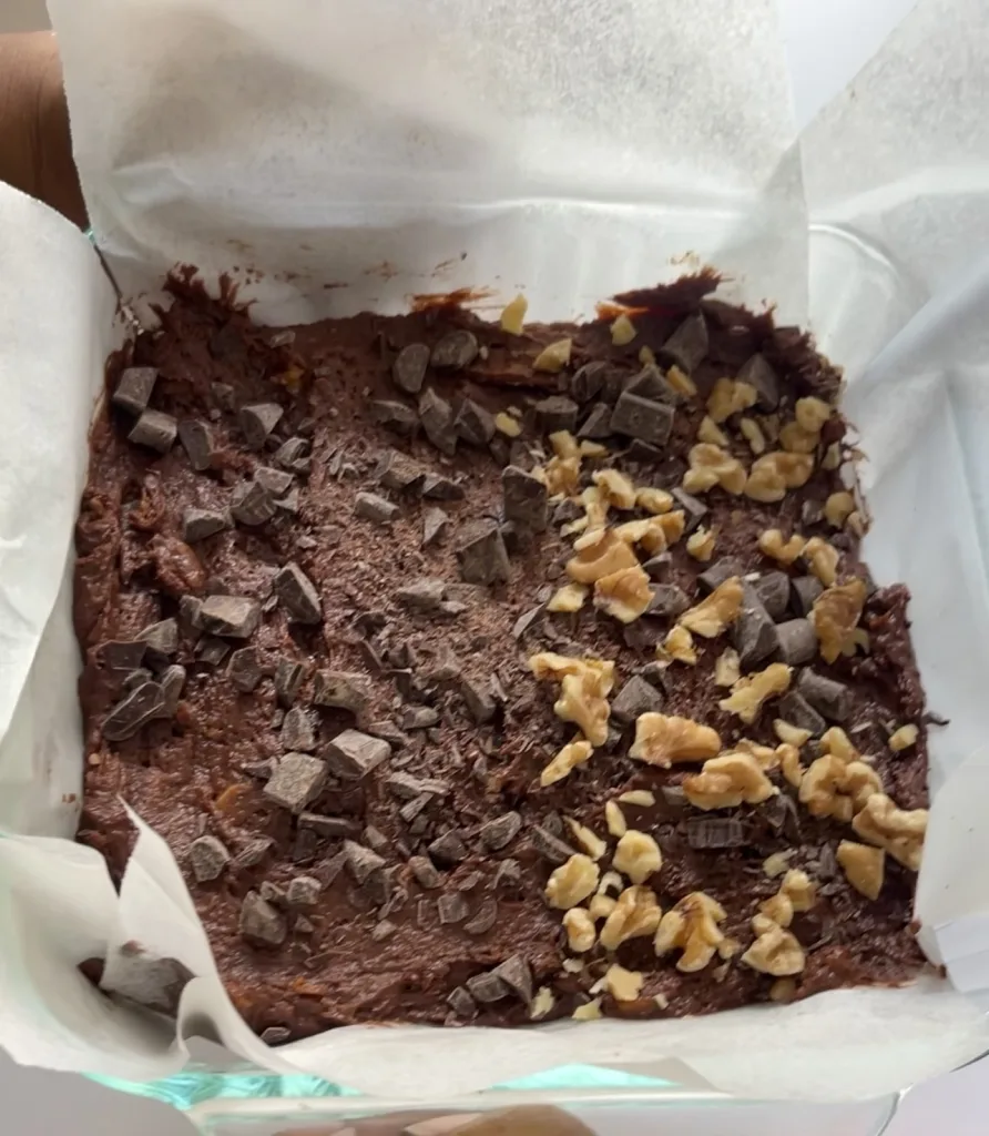 sweet potato brownie batter in parchment paper-lined baking dish with half covered in just chocolate chunks and the other half covered in chocolate chunks and walnuts