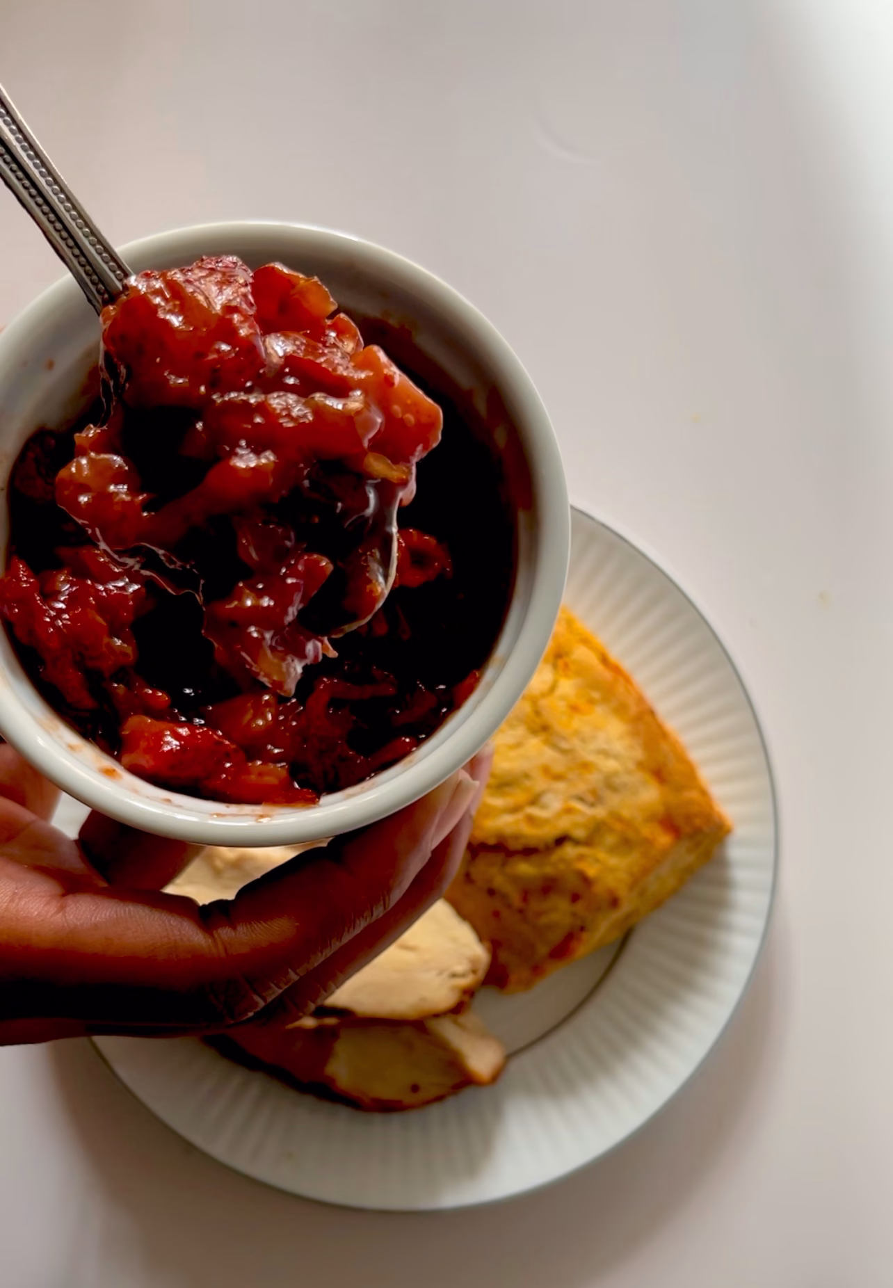 strawberry bacon and onion jam in a white ramekin with spoon and biscuit with turkey in the background