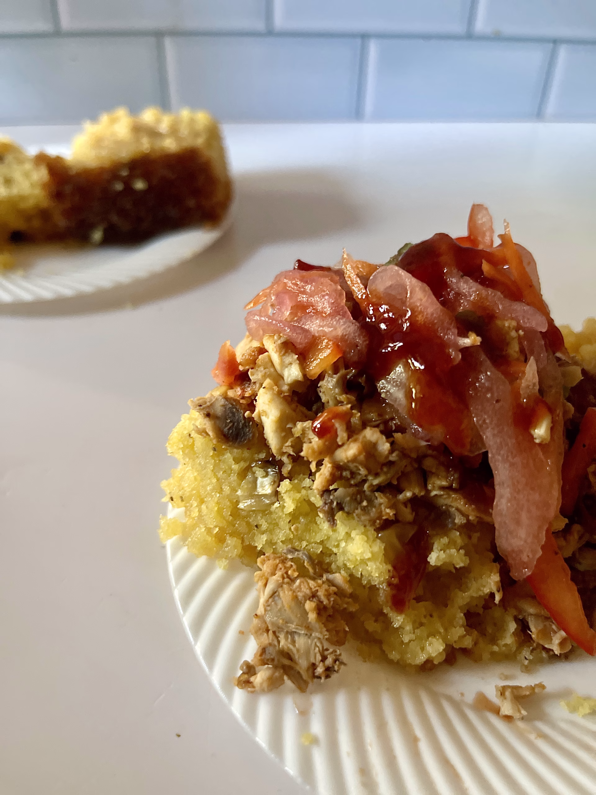 an open face cornbread biscuit with smoked chicken watermelon bbq sauce and watermelon rind relish on a small white plate